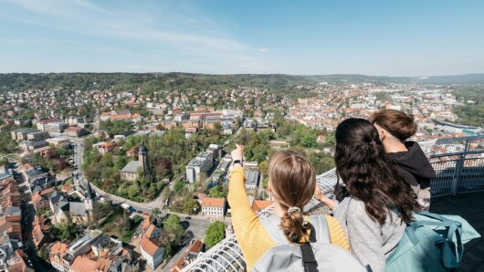 Drei Studierende stehen auf dem Jentower und zeigen auf die Stadt Jena